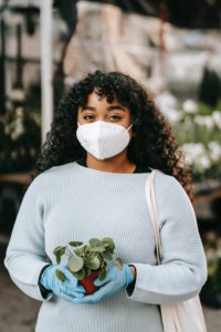 Photo of in mask and gloves holding a potted plant by Uriel Mont from Pexels